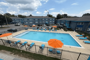 A pool surrounded by chairs and umbrellas with apartment buildings in the background.